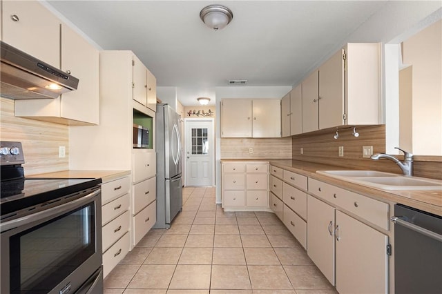 kitchen featuring visible vents, a sink, under cabinet range hood, backsplash, and appliances with stainless steel finishes