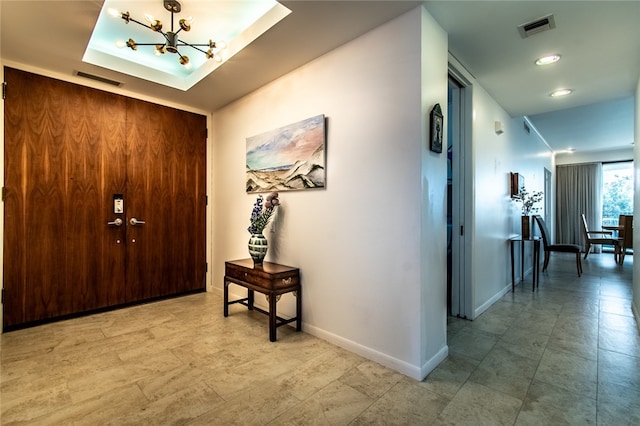 foyer entrance with a raised ceiling and a notable chandelier