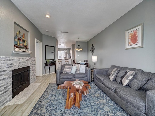 living area with light wood-style floors, visible vents, a fireplace, and an inviting chandelier