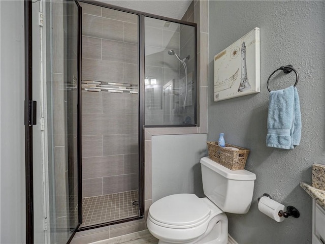 full bath featuring a stall shower, a textured wall, vanity, and toilet