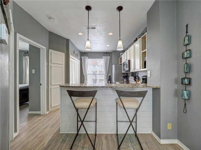 kitchen featuring a peninsula, light wood-style floors, a breakfast bar area, and stainless steel appliances