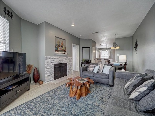 living area featuring light wood-type flooring, plenty of natural light, visible vents, and a stone fireplace