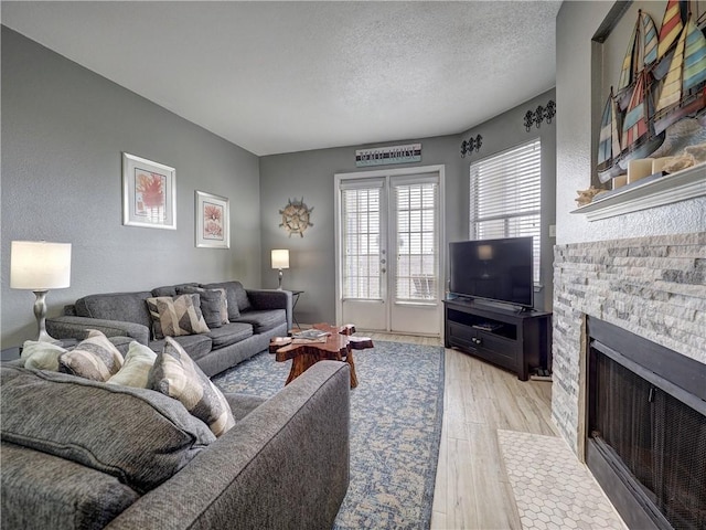 living room with light wood-style flooring, french doors, a textured ceiling, and a stone fireplace