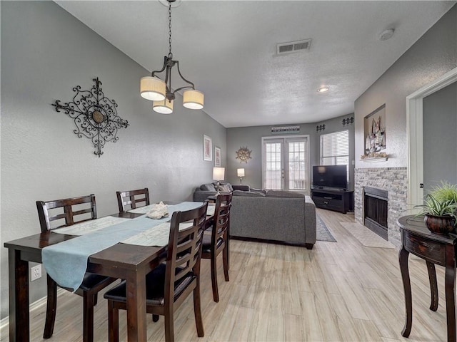 dining space with light wood-type flooring, french doors, a fireplace, and visible vents