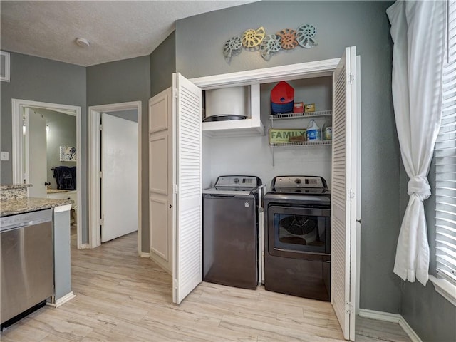 laundry area featuring light wood-style floors, a textured ceiling, washer and dryer, laundry area, and baseboards