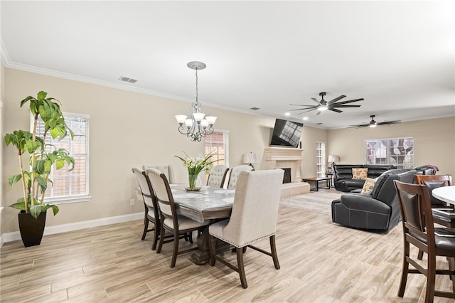 dining room featuring ceiling fan with notable chandelier, a healthy amount of sunlight, a fireplace, and light wood finished floors