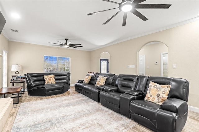 living area with visible vents, ceiling fan, ornamental molding, light wood-style flooring, and arched walkways