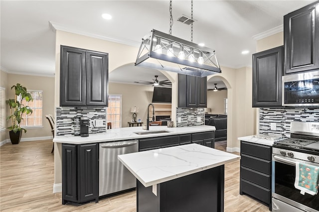 kitchen featuring ornamental molding, appliances with stainless steel finishes, arched walkways, a ceiling fan, and a sink