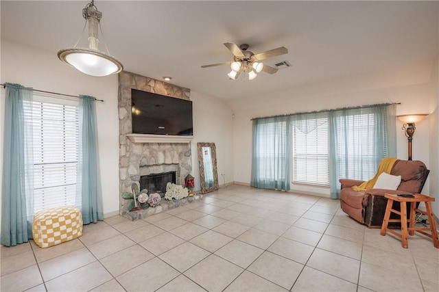 living room with light tile patterned flooring, ceiling fan, and a stone fireplace