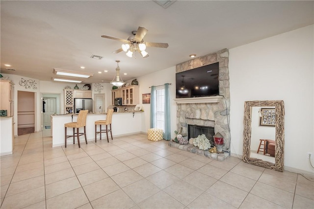 living room featuring a stone fireplace, light tile patterned floors, and ceiling fan