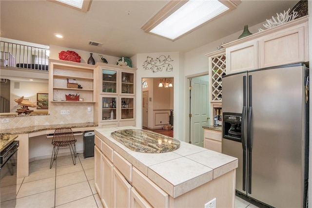 kitchen with light tile patterned flooring, built in desk, dishwasher, a center island, and stainless steel refrigerator with ice dispenser