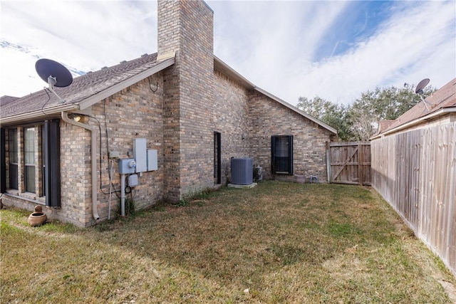 view of side of property with central AC unit, a chimney, a gate, fence, and a yard