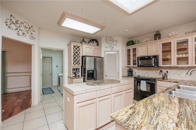 kitchen with light countertops, glass insert cabinets, a sink, a kitchen island, and black appliances