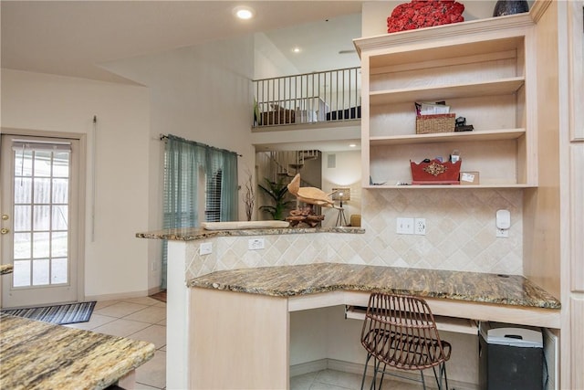 kitchen featuring built in desk, tasteful backsplash, light tile patterned floors, kitchen peninsula, and light stone countertops