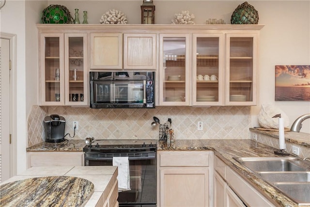 kitchen with glass insert cabinets, a sink, black appliances, and tasteful backsplash