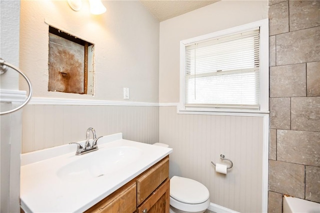 bathroom with a textured ceiling, toilet, a washtub, a wainscoted wall, and vanity