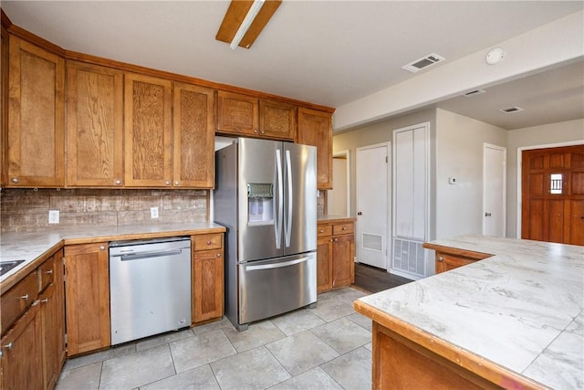 kitchen with visible vents, brown cabinetry, decorative backsplash, appliances with stainless steel finishes, and light countertops