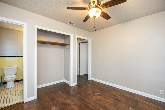 unfurnished bedroom with dark wood-style floors, tile walls, a closet, visible vents, and a textured ceiling