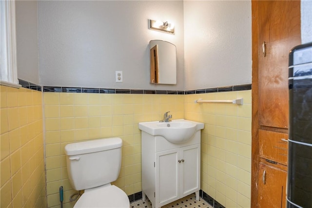 half bathroom featuring toilet, wainscoting, tile walls, and vanity