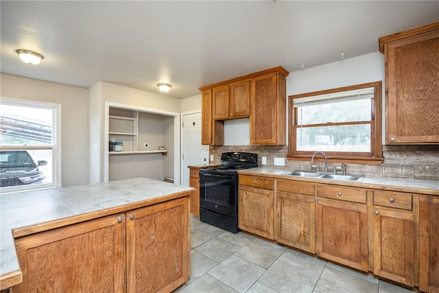 kitchen with a wealth of natural light, light countertops, brown cabinetry, a sink, and black / electric stove