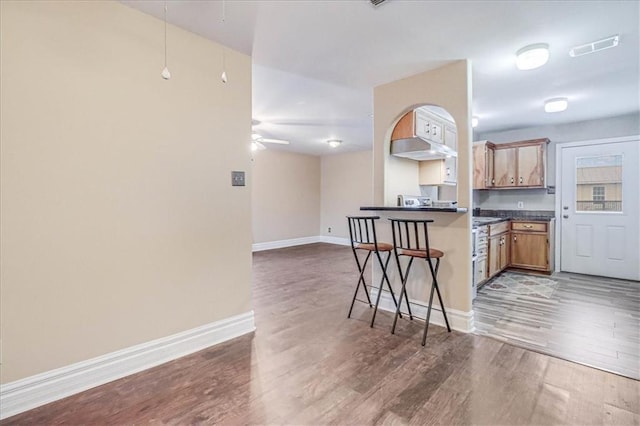 kitchen with dark countertops, ceiling fan, baseboards, light wood-type flooring, and a kitchen breakfast bar