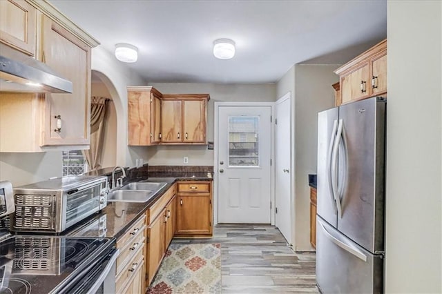 kitchen featuring light wood-style flooring, arched walkways, a sink, appliances with stainless steel finishes, and dark countertops