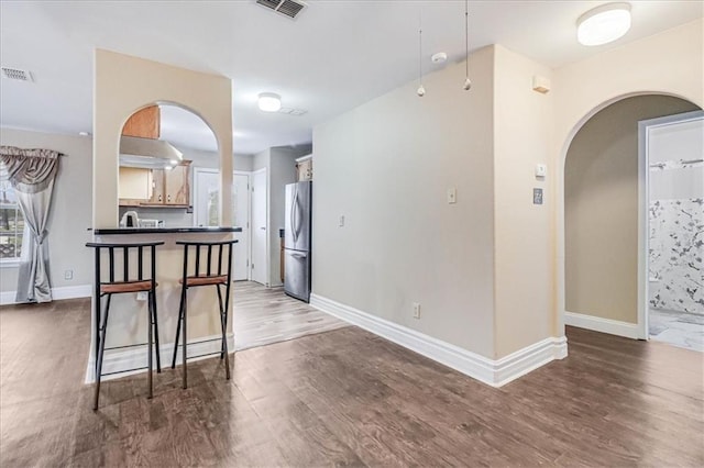 kitchen with dark countertops, wood finished floors, freestanding refrigerator, arched walkways, and baseboards