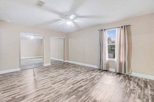 unfurnished bedroom with visible vents, two closets, baseboards, and wood finished floors