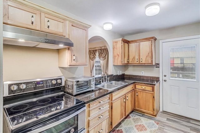 kitchen with under cabinet range hood, double oven range, dark countertops, and a sink