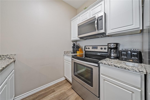 kitchen with appliances with stainless steel finishes, light stone counters, white cabinets, and light wood-type flooring