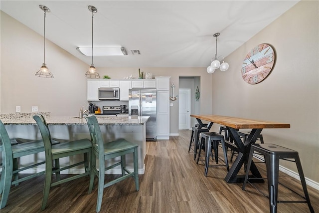 kitchen with white cabinetry, hardwood / wood-style floors, stainless steel appliances, light stone countertops, and a kitchen bar