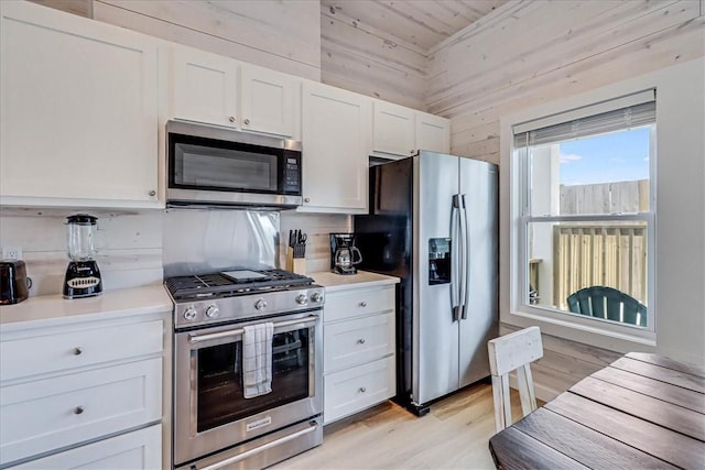 kitchen featuring wooden walls, light wood-type flooring, white cabinetry, and appliances with stainless steel finishes