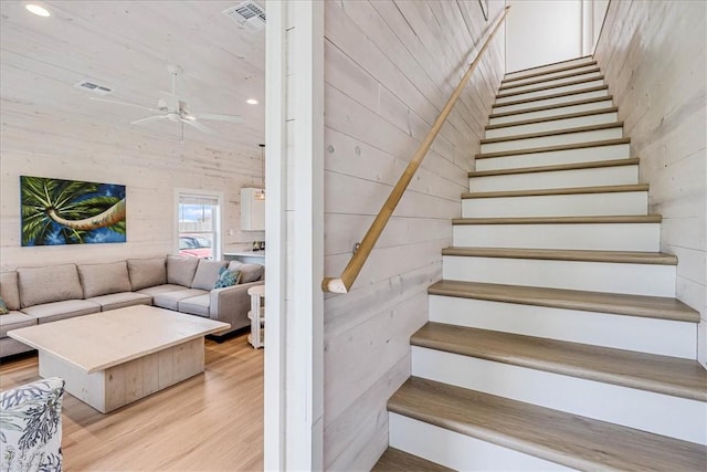 stairway featuring hardwood / wood-style floors, a towering ceiling, ceiling fan, and wooden walls