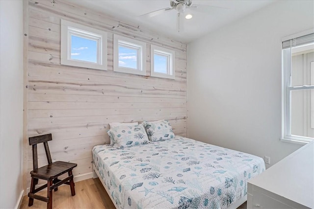 bedroom with ceiling fan, wood walls, and light wood-type flooring