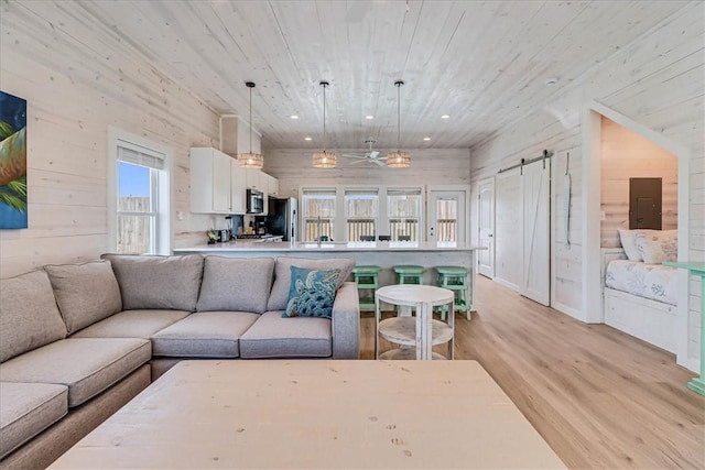 living room with wooden walls, a barn door, light wood-type flooring, and electric panel