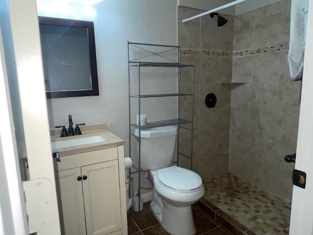 bathroom featuring toilet, a tile shower, vanity, and tile patterned floors