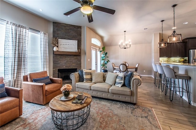 living room with ceiling fan with notable chandelier, a fireplace, and light hardwood / wood-style floors