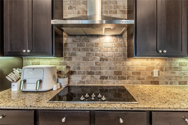 kitchen featuring black electric cooktop, dark brown cabinetry, wall chimney exhaust hood, and light stone countertops