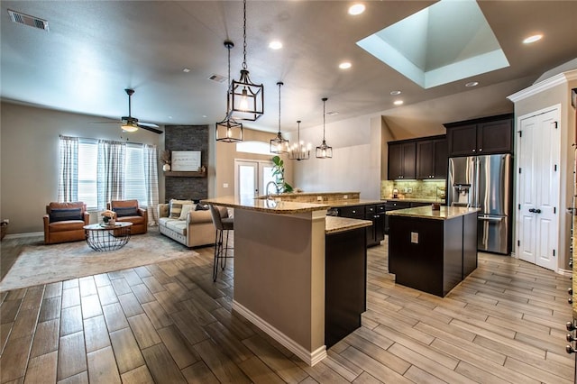 kitchen with stainless steel refrigerator with ice dispenser, a kitchen breakfast bar, pendant lighting, light stone countertops, and a kitchen island with sink