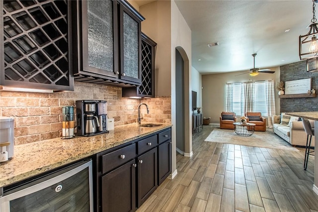 kitchen with wine cooler, sink, light stone counters, dark brown cabinets, and pendant lighting