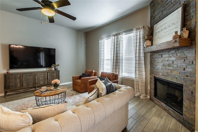 living room with ceiling fan, a stone fireplace, and light wood-type flooring