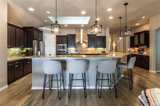 kitchen featuring a spacious island, stainless steel appliances, hanging light fixtures, and wall chimney range hood