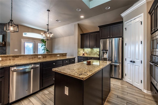 kitchen featuring vaulted ceiling, a kitchen island, appliances with stainless steel finishes, pendant lighting, and light stone countertops