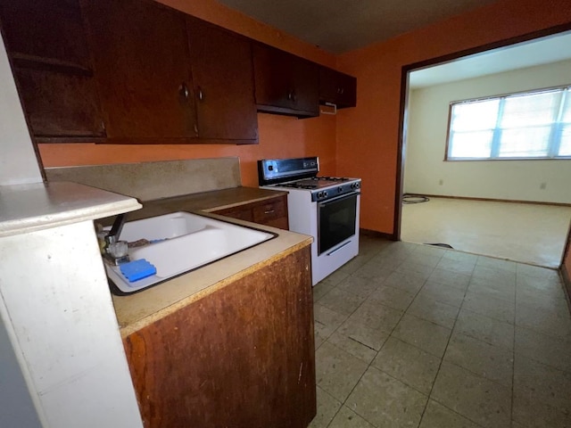 kitchen with dark brown cabinetry, ventilation hood, sink, and white range with gas stovetop