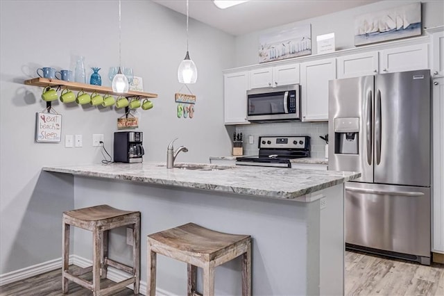 kitchen featuring a breakfast bar, backsplash, appliances with stainless steel finishes, white cabinetry, and a sink