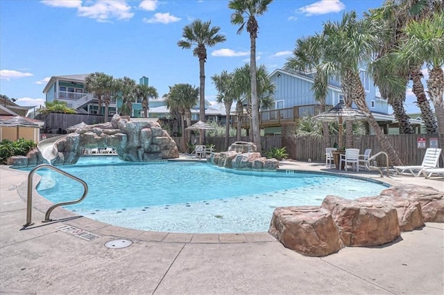 community pool featuring a patio area, fence, and a water slide