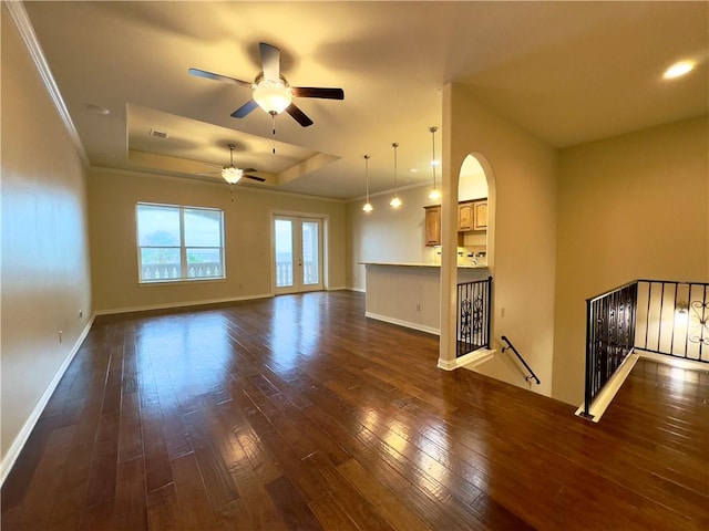 unfurnished living room featuring a raised ceiling, ceiling fan, dark hardwood / wood-style flooring, and ornamental molding