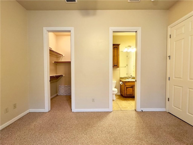 unfurnished bedroom with ensuite bath, sink, light colored carpet, a walk in closet, and a closet