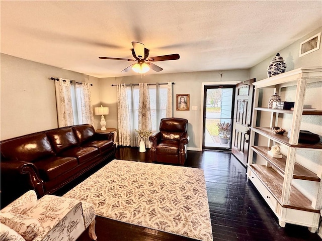 living room featuring baseboards, visible vents, a ceiling fan, dark wood-type flooring, and a textured ceiling