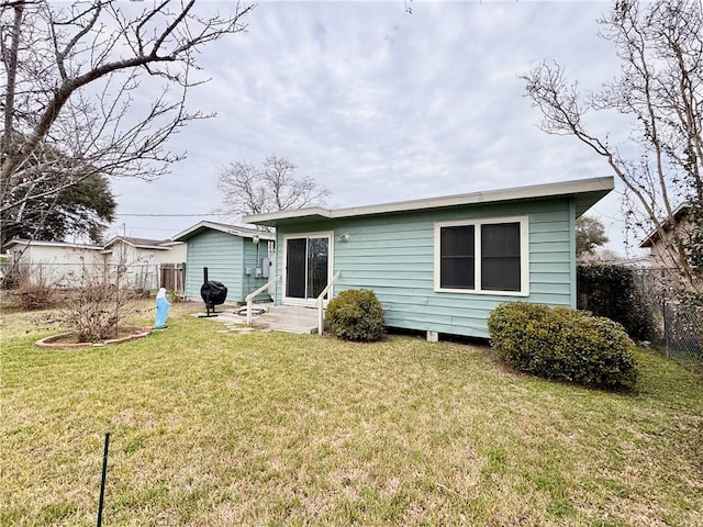 back of property with entry steps, a lawn, and fence